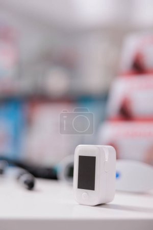 Téléchargez les photos : Oxymètre médical debout sur la table dans une pharmacie vide prête à être utilisée par le client, appareil numérique pour mesurer la saturation en oxygène. Droguerie remplie de médicaments, vitamines et produits pharmaceutiques - en image libre de droit