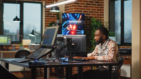 Téléchargez les photos : Développeur web afro-américain travaillant dans un bureau artistique pour créer du contenu CGI sur des logiciels 3D, des compétences numériques. Designer d'agence créative utilisant une interface professionnelle pour développer des infographies. - en image libre de droit