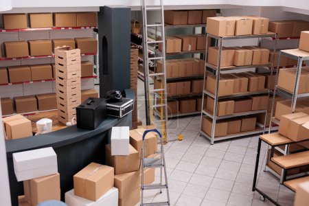 Photo for Empty huge distribution warehouse equipped with high shelves fill with cardboard boxes, online orders ready for delivering. Interior of new large and modern storehouse space with nobody in it - Royalty Free Image