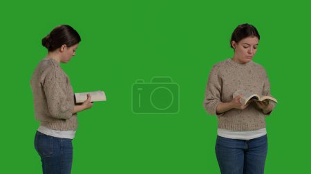 Foto de Focused adult holding action book and reading in studio, enjoying novel chapter with story. Woman standing over isolated greenscreen backdrop, read tale on camera as leisure activity. - Imagen libre de derechos