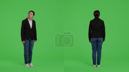Photo for Positive company worker standing in studio over greenscreen backdrop, posing on camera with office suit. Young businesswoman with corporate job acting optimistic and curious, full body. - Royalty Free Image