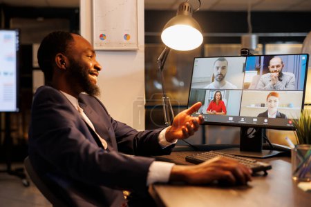 Photo for Smiling executive manager having remote conversation with team discussing marketing strategy during online videocall meeting. Diverse coworkers working at company growth report in office - Royalty Free Image