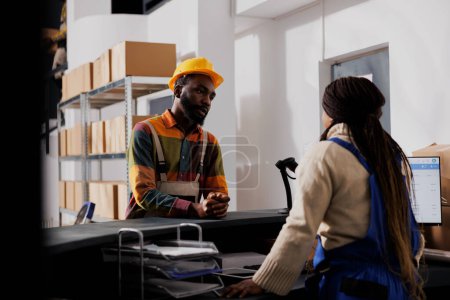 Photo for Warehouse workers standing at counter desk discussing shipment management. Two african american post office employees talking about package delivery at checkout in storage room - Royalty Free Image