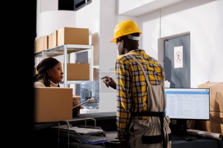 Photo for African american woman warehouse supervisor talking with manager at reception desk. Distribution manager coordinating packages shipment while discussing logistics stock supply chain - Royalty Free Image