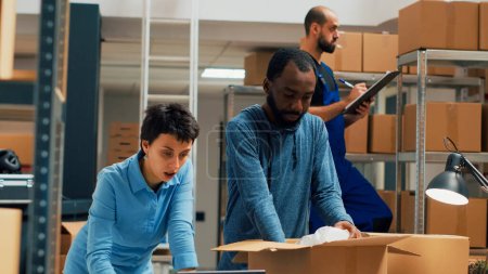 Photo for Diverse team of business owners packing order for shipping, using cardboard boxes and merchandise. Man and woman working on supply chain and logistics, quality control. Handheld shot. - Royalty Free Image