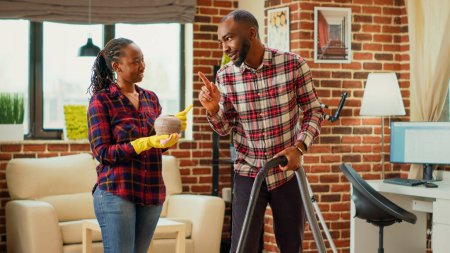 Photo for Life partners doing spring cleaning together in living room, focused people doing household chores. Man vacuuming floors and woman sweeping dust off of furniture on shelves, housework. - Royalty Free Image