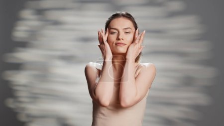 Photo for Confident woman using moisturizing facial cream for beauty routine, creating new ad campaign for glowing products. Cheerful sensual girl posing on camera to advertise nourishing luminous look. - Royalty Free Image