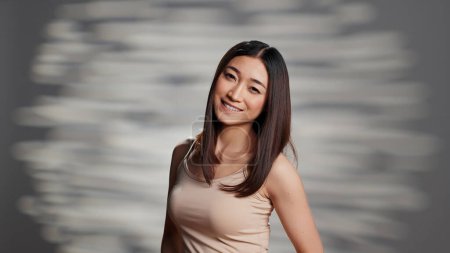 Téléchargez les photos : Happy beautiful lady embracing imperfections for ad, feeling flawless with luminous natural skin in studio. Asian woman with glowing look promoting body acceptance and self confidence. - en image libre de droit