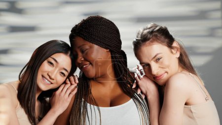 Interrassische Damengruppe, die im Studio um Körperakzeptanz wirbt und Selbstbewusstsein und Körperpflege zeigt. Beauty-Models mit strahlendem Look posieren für Hautpflege-Kampagne mit verschiedenen Frauen.