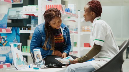 Téléchargez les photos : Health specialist giving medical advice and pills to girl, recommending medicaments from pharmacy store. Young female pharmacist explaining about drugs treatment to customer. Handheld shot. - en image libre de droit