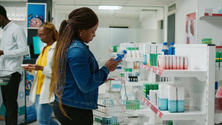 Téléchargez les photos : Female customer checking pharmaceutical products from drugstore racks, looking to buy medicaments and supplements for healthcare. Young adult taking medicine and drugs from pharmacy. - en image libre de droit