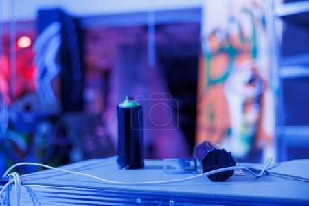 Photo for Aerosols containers in abandoned urban building illuminated by bright purple neon lights. Bottles and cans with spray paint glowing in the dark, fluorescent lights in ghetto space. Close up. - Royalty Free Image