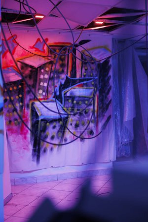 Foto de Espacio urbano abandonado con luces de neón púrpura y rosa, mostrando polvo en las paredes, almacén abandonado con estructura desmoronada cubierta de pintura de graffiti desordenada. Lugar con luces fluorescentes. - Imagen libre de derechos