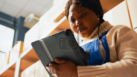 Photo for Depot worker scanning barcodes with scanner, checking carton boxes in storage room with tablet. Young woman doing stock inventory or logistics, preparing retail store distribution. Handheld shot. - Royalty Free Image
