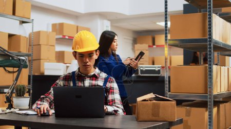 Photo for Young man planning order shipment in storehouse, using laptop to do stock logistics. Storage room employee working with products and merchandise, supply chain distribution packs. - Royalty Free Image