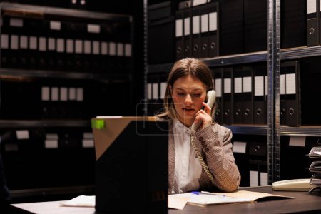 Photo for Bookkeeper discussing accountancy report with manager using landline phone, working overhours at management research in storage room. Repository worker checking bureaucracy record - Royalty Free Image