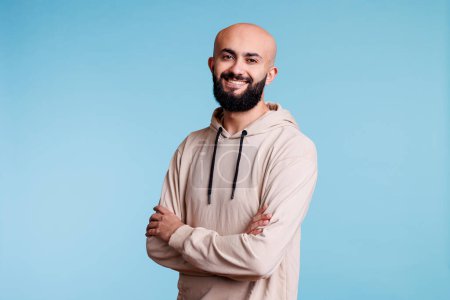 Photo for Cheerful smiling arab man posing confidently with folded arms portrait. Young happy arabian person wearing casual hoodie while standing with crossed hands and looking at camera - Royalty Free Image