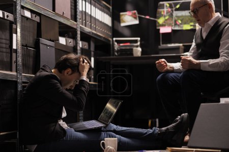 Photo for Overworked investigators working overhours at criminal case in arhive room, analyzing criminology documents. Tired private detectives looking at crime scene evidence, discussing victim report - Royalty Free Image