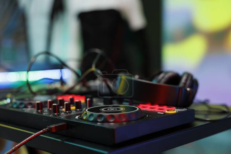 Dj controller with jog wheels, knobs and buttons for electronic music mixing at nightclub stage. Musician console panel and headphones for live performance in club close up