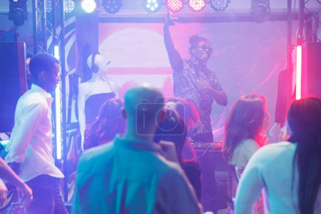 Foto de Dj actuando en el escenario y entretenida multitud bailando en discoteca. Joven músico afroamericano tocando música electrónica y mezclando sonidos en una fiesta de discoteca en el club - Imagen libre de derechos
