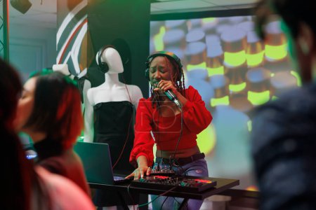 Woman singer mixing techno sounds with dj station on stage while performing at nightclub party. African american musician wearing headphones singing in microphone in club