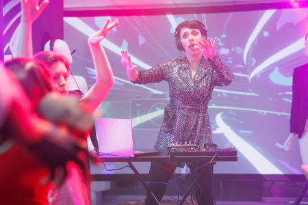 Téléchargez les photos : Femme mélangeant le son avec la station de DJ sur scène et jouant pour la foule dans la boîte de nuit. Fille se produisant pour les gens dansant et s'amusant sur la piste de danse au festival de musique électronique dans le club - en image libre de droit