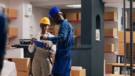 Photo for Diverse people working with merchandise in boxes, planning order distribution for goods shipment. Two depot employees looking at packages filled with stock merchandise. Tripod shot. - Royalty Free Image