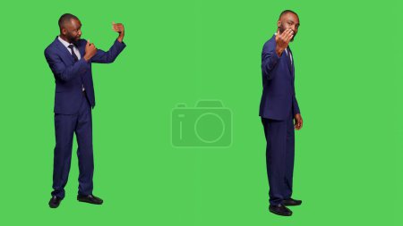 Photo for Corporate employee asking someone to come over, waving hand to call people over and accompany him. Male office worker wearing formal suit over full body green screen backdrop. - Royalty Free Image