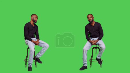 Photo for African american man on chair posing with confidence, sitting over full body green screen backdrop. Young male model feeling optimistic and waiting for something in studio, natural person. - Royalty Free Image