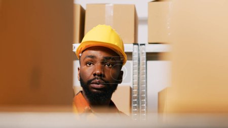 Photo for Male employee counting boxes of products in warehouse, reviewing merchandise cargo on tablet to prepare order shipment. Manager checking stock inventory and logistics. Handheld shot. - Royalty Free Image