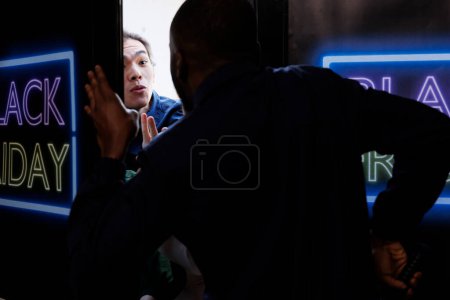 Foto de Joven asiático tratando de entrar en la tienda al por menor el Viernes Negro antes del horario de apertura, comprador loco luchando y discutiendo con guardia de seguridad mientras está de pie en la entrada del centro comercial - Imagen libre de derechos