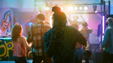 Photo for Male adult answering phone call at party, trying to have remote chat at nightclub event. Young man trying to talk on smartphone, partying with electronic music on dance floor. Handheld shot. - Royalty Free Image