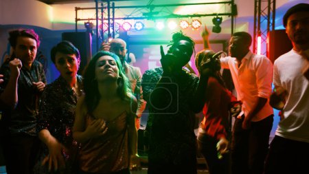Téléchargez les photos : Point de vue de divers adultes faisant la fête au club, faire des mouvements de danse funky à la caméra lors de la fête disco. Des hommes et des femmes qui font preuve de talent en musique électronique dans une boîte de nuit, dansant ensemble. Coup de main. - en image libre de droit