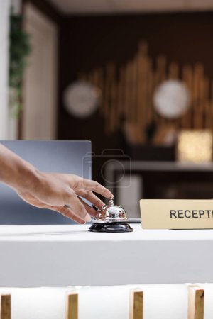 Téléchargez les photos : Homme sonne cloche de service au comptoir, demandant l'aide des employés de l'hôtel à la réception. Invité à la recherche d'une réceptionniste dans le hall pour aider à la réservation des chambres. Gros plan. - en image libre de droit