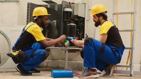 Efficient technicians assembling professional pressure manifold gauges to check liquids and gases in hvac system while seasoned mechanic cleans layer of built up dirt and dust in air conditioner