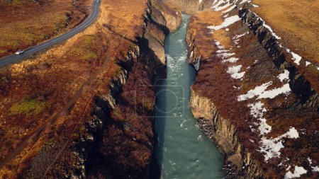 Foto de Drone shot of gullfoss river cascade, majestuoso arroyo de agua que fluye entre coloridas colinas nevadas y campos. Naturaleza islandesa y paisaje cerca de la cascada. Movimiento lento. - Imagen libre de derechos