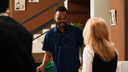 Photo for Diverse couple waiting to register at tropical seaside hotel, travelling on summer vacation. International tourists talking to front desk staff in lobby at exotic resort reception. - Royalty Free Image