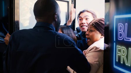 Photo for Out of control crowd of mad people breaking into shopping mall during black friday event, knocking agent to hurry inside clothing store and benefit from best deals and promotions. - Royalty Free Image