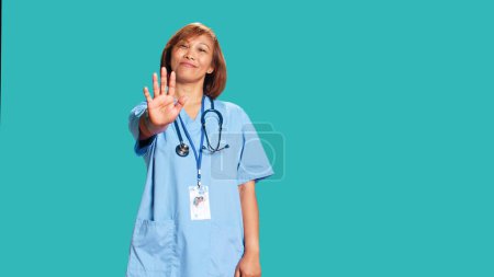 Photo for Adamant uncompromising healthcare expert throwing stop hand sign, unhappy with work conditions. Assertive asian nurse doing halt gesturing, isolated over blue studio background - Royalty Free Image