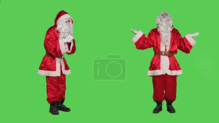 Photo for Santa claus praying to god with hands in a prayer, posing over full body greenscreen in studio. Spiritual religious character with festive red suit, talking to jesus advertising christmas holiday. - Royalty Free Image