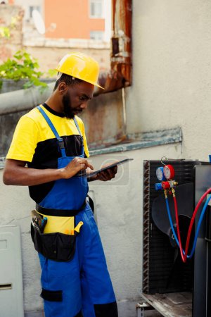Photo for Expert repairman doing condenser investigations, filter replacements and necessary fixes to prevent major breakdowns. Proficient worker checking up hvac system, writing findings on clipboard - Royalty Free Image