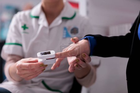 Téléchargez les photos : Travailleur apothicaire mettant oxymètre de pouls sur le doigt du patient pour le diagnostic des maladies cardiologiques. Assistante pharmaceutique examinant la santé cardiaque du client en pharmacie et mesurant le taux d'oxygène dans le sang - en image libre de droit