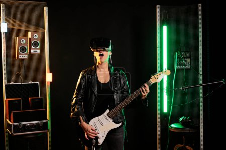 Photo for Rebel musician playing rock song using electric guitar while wearing virtual reality headset during music session in sound studio. Performer with goggles having grunge concert simultation - Royalty Free Image