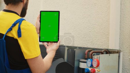 Téléchargez les photos : Mécanicien commander de nouveaux composants sur écran vert maquette tablette pour climatiseur hors service après avoir terminé le dépannage. Expert à la recherche en ligne de pièces de rechange de système hvac - en image libre de droit