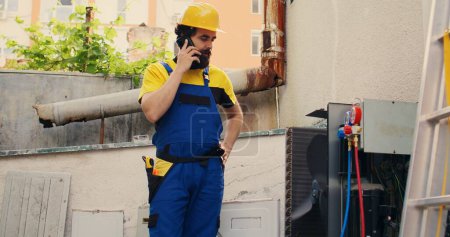 Photo for Skilled engineer on the phone with home owner after finishing hvac system repairments. Expert repairman calling client to inform him about built up layers of dirt found on air conditioner unit - Royalty Free Image