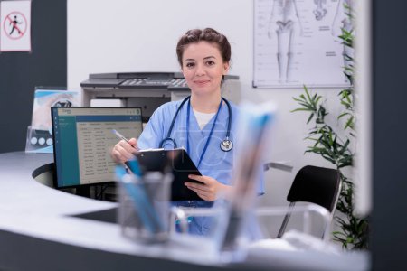 Photo for Smiling nurse holding clipboard checking medical report while working at patient medication treatment after checking disease diagnosis in hospital reception. Health care service and concept - Royalty Free Image