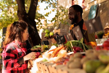 Photo for Diverse people talking about organic bio products at farmers market, various natural farming produce. Young man and woman looking at locally grown fresh eco fruits and veggies. - Royalty Free Image