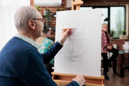 Photo for Senior man sitting at easel drawing vase with pencil, attending social art classes, awakening artistic side in retirement, exploring and discovering new passions. Mature student practicing sketching - Royalty Free Image