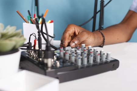 Foto de Hombre de mano girando la perilla en el equipo de control de sonido en el estudio de cerca. blogger afroamericano usando equipo profesional de consola de mezclador de música mientras crea contenido digital para vlog - Imagen libre de derechos