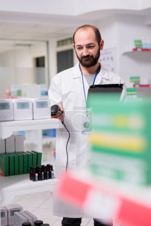 Foto de Portrait of pharmacist checking medication list on tablet computer while scanning pills packages using store scanner in pharmacy. Drugstore worker is responsible for organizing and labeling the drugs - Imagen libre de derechos